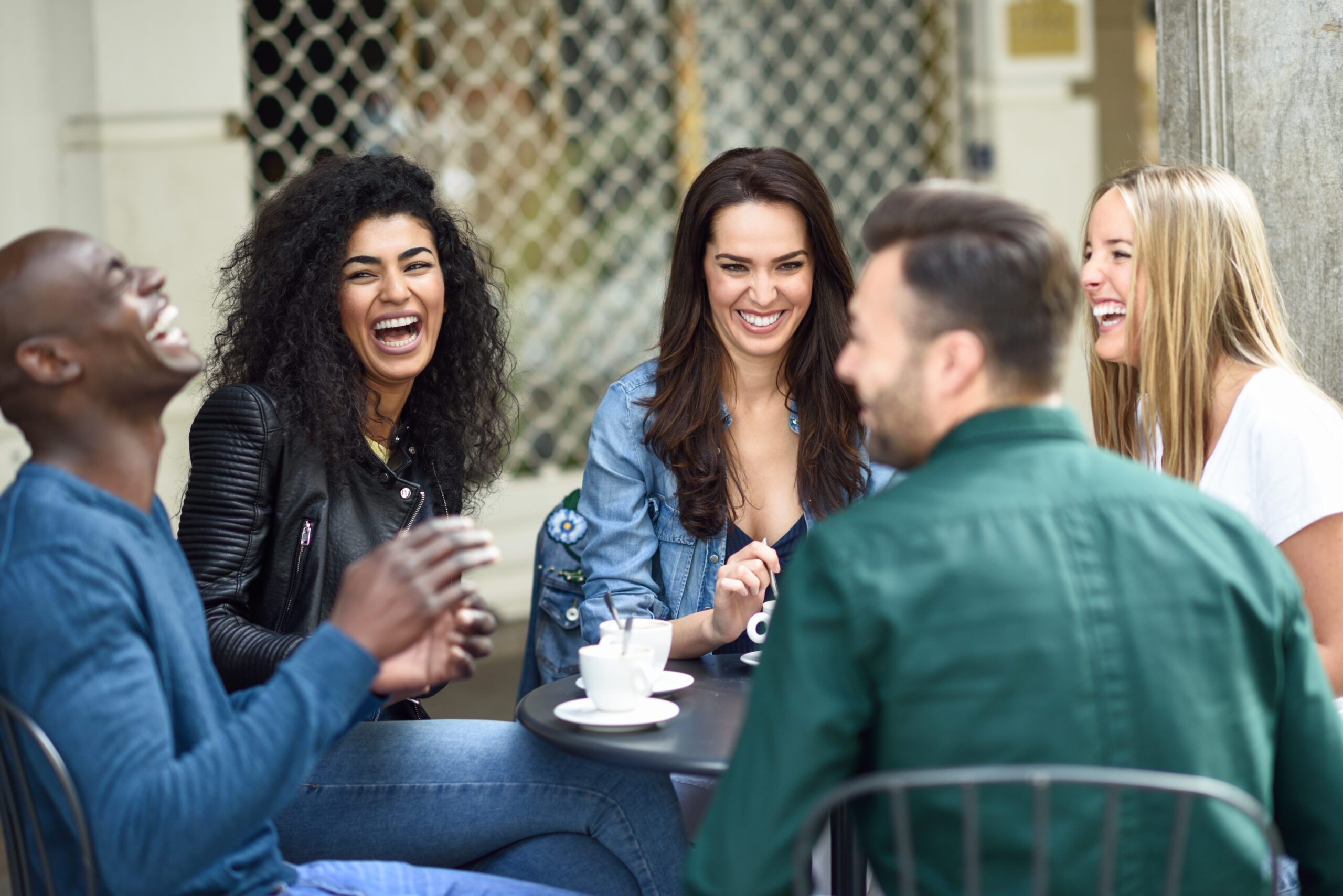 Multiracial group of five friends having a coffee together. Three women and two men at cafe, talking, laughing and enjoying their time. Lifestyle and friendship concepts with real people models